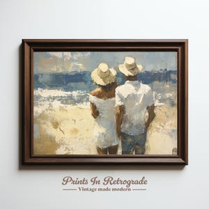 May include: A framed painting showing a couple on a beach, looking out to sea. They are dressed in white and wearing hats. The artwork uses blues, whites, and beige, with visible brushstrokes. The frame is dark brown. The text "Prints In Retrograde - Vintage made modern" is at the bottom.