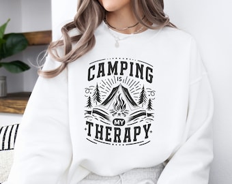 May include: White sweatshirt with black text that reads "Camping is my therapy" with a graphic of a campfire and tent.