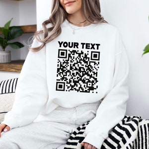 May include: White sweatshirt with a black and white QR code and the text "YOUR TEXT" printed on the front.