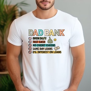 May include: White t-shirt with a graphic that says "DAD BANK" and a list of services offered, including "Open 24/7", "Fast Cash", "No Credit Checks", "Same Day Loans", and "0% Interest on Loans".