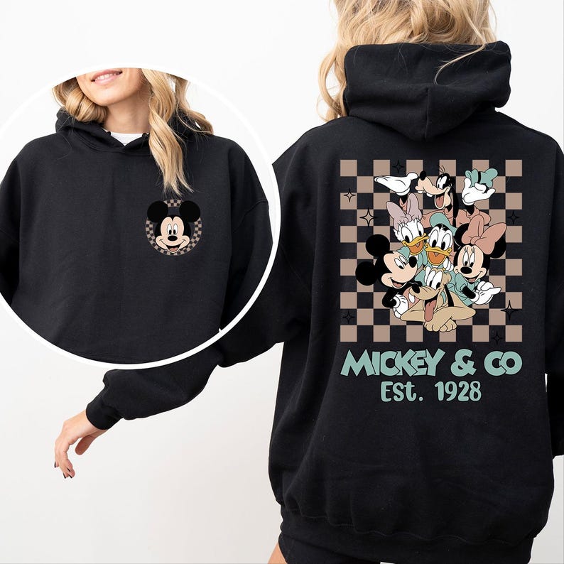 K&ouml;nnte beinhalten: Schwarzer Kapuzenpullover mit einem Mickey Mouse-Motiv auf der Vorderseite und einer Gruppe von Disney-Figuren auf der R&uuml;ckseite. Das R&uuml;ckendesign ist vor einem braunen und beigefarbenen Karomuster platziert, mit dem Aufdruck "Mickey & Co Est. 1928".