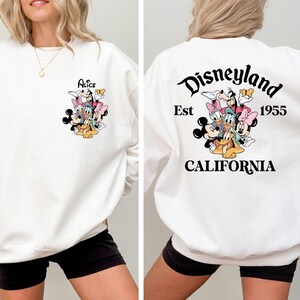 May include: White sweatshirt featuring a colorful graphic of Disney characters on the front and back. The front displays the name "Alice" above the characters. The back of the sweatshirt says "Disneyland Est 1955 California".