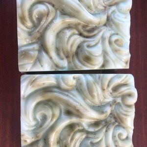 May include: Two bars of handmade soap with a swirling green and white design. The soap has a marbled appearance.