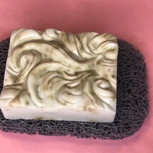 May include: A white and green swirl design soap bar on a gray textured soap dish.