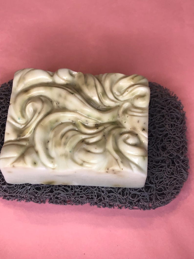 May include: A white and green swirl design soap bar on a gray textured soap dish.
