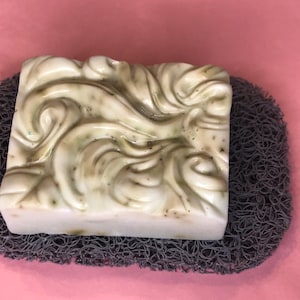May include: A white and green swirl design soap bar on a gray textured soap dish.