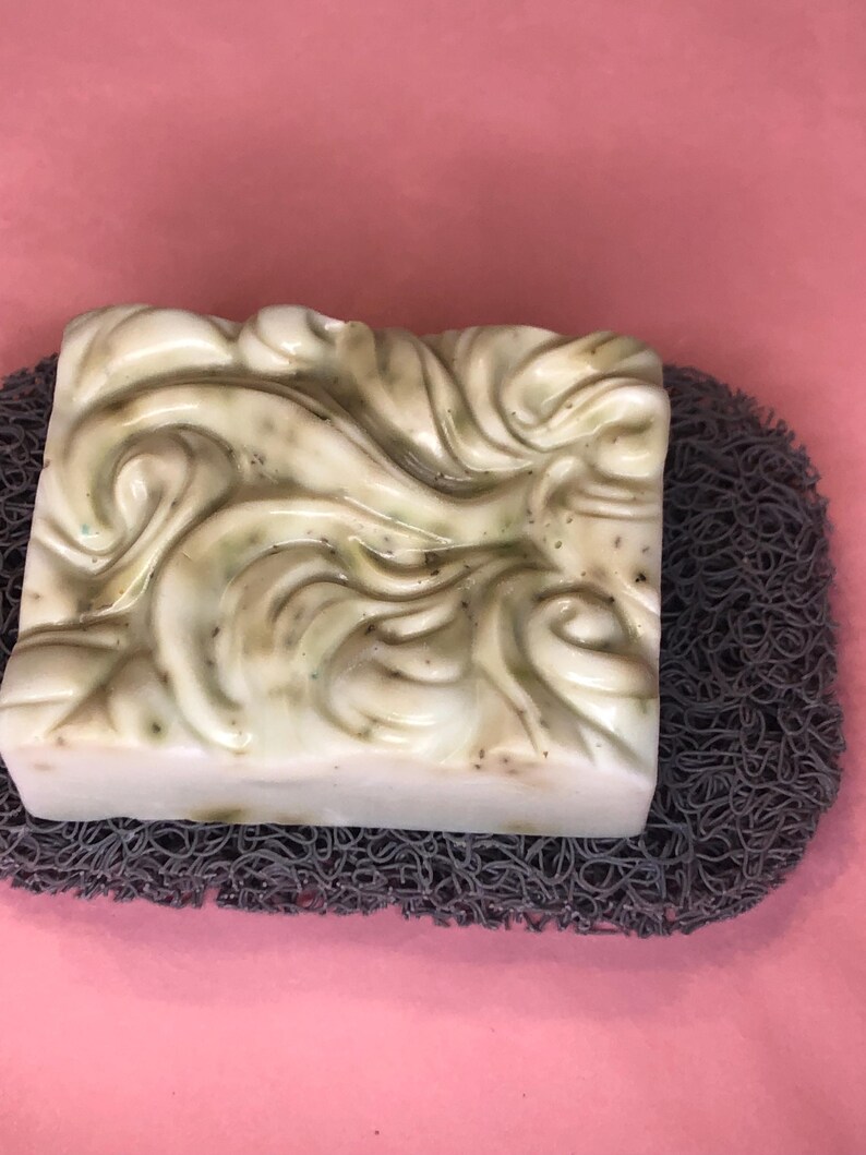 May include: A white and green swirl design soap bar on a gray textured soap dish.