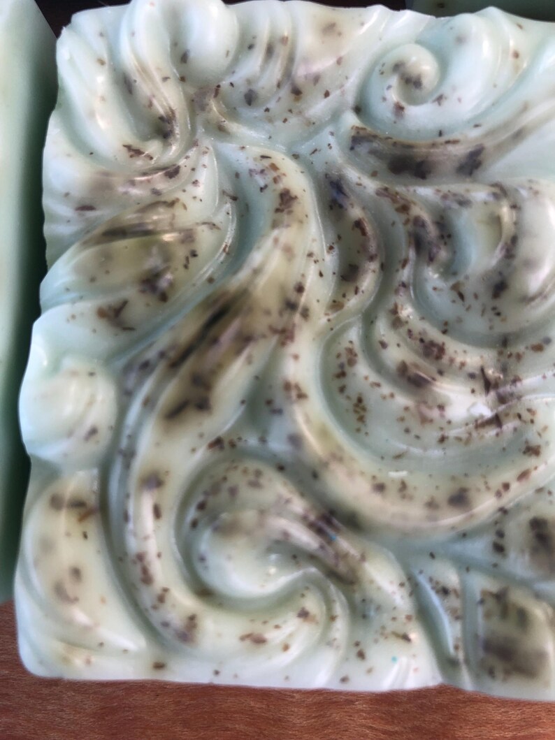 May include: A close-up of a light green bar of soap with a swirl design and brown flecks throughout.
