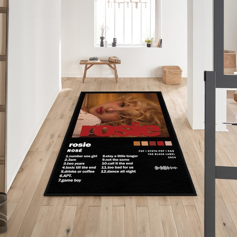 May include: Black rectangular rug featuring the album cover of "Rosie" by Ros&eacute;. The design includes a photo of Ros&eacute;, the album title, tracklist, and label information. The rug is placed on a wooden floor.