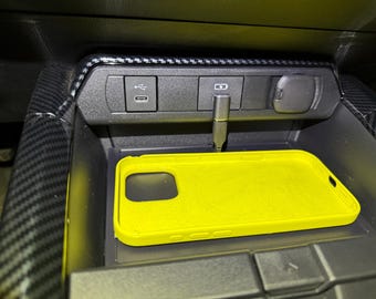 May include: A yellow phone case sits in a car's center console. The console has a USB port, a button, and a small compartment.