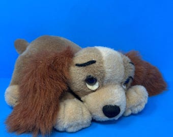 Peluche Disney di Lilli e il Vagabondo, cagnolina di Lilli e il Vagabondo, marrone chiaro con lunghe orecchie pelose, sdraiata.