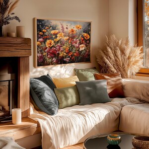 Op de afbeelding: Een woonkamer met een bank bekleed met witte linnen stof. De bank heeft verschillende kussens in verschillende kleuren en texturen, waaronder groen, bruin en grijs. Een schilderij met een bloemstuk met oranje, gele en rode bloemen hangt aan de muur boven de bank.