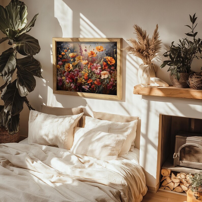 Op de afbeelding: Een ingelijst schilderij van een kleurrijk bloemstuk met verschillende bloemen, waaronder klaprozen, in tinten rood, oranje, geel en roze. Het schilderij hangt aan een witte muur boven een bed met wit linnen beddengoed.