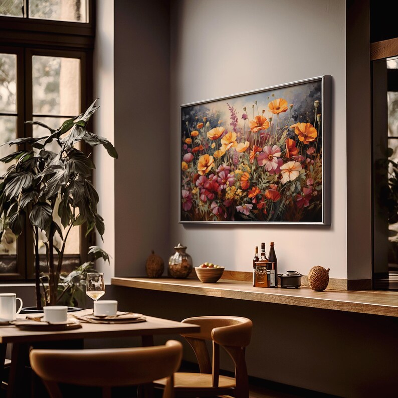 Op de afbeelding: Een ingelijst schilderij van een kleurrijk bloemstuk met verschillende bloemen, waaronder klaprozen, madeliefjes en wilde bloemen. Het schilderij is geplaatst tegen een lichtblauwe achtergrond met een zacht, wazig effect. De lijst is zilverkleurig en heeft een eenvoudig, modern ontwerp.
