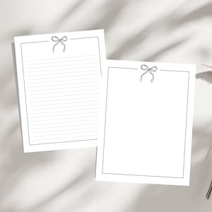 May include: Two white sheets of stationery. One sheet has horizontal lines for writing, the other is blank. Both sheets have a black bow design at the top center and a black border.