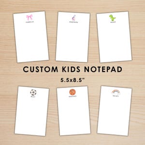 May include: A collection of six white custom kids notepads, each with a different design and name. The notepads are 5.5 x 8.5 inches. The top of each notepad features a small graphic: a bow, a unicorn, a dinosaur, a soccer ball, a basketball, and a rainbow.