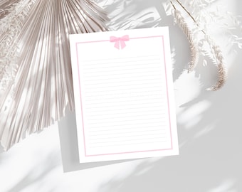 Peut inclure: Papier à lettres blanc ligné avec une bordure rose et un nœud rose en haut. Le papier est entouré d'éléments décoratifs, dont un grand éventail texturé et des tiges florales séchées, le tout sur fond blanc.