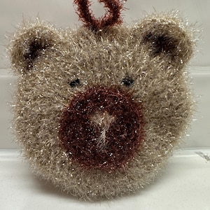 May include: A brown and gold sparkly knitted bear with a red knitted nose and a red knitted halo on top of its head.