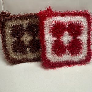May include: Two crocheted dishcloths, one brown and one red with a white cross in the center.