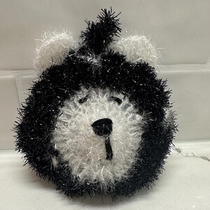 May include: A black and white crocheted bear-shaped bath sponge with a fluffy texture.