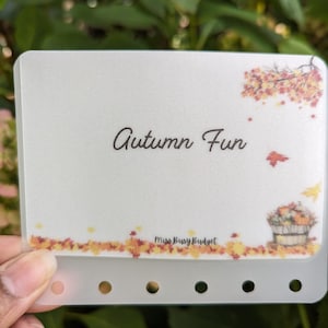 May include: A white planner page with a fall theme. The page has a brown title that says "Autumn Fun" and a small illustration of a basket of pumpkins and fall leaves. The bottom of the page has a line of fall leaves and the text "Miss Busy Budget".