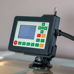 May include: A black and gray control panel with a screen, buttons, and a suction cup mount. The panel has a green and red button, a directional pad, and a screen with a grid pattern. The panel is connected to a black cable.
