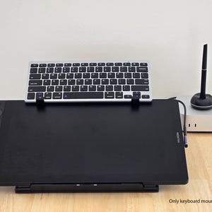 May include: A black drawing tablet with a silver keyboard mounted above it. A silver computer and a black stylus are to the right. The text "Only keyboard mount is included" is at the bottom.