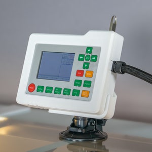 May include: A white control panel with a green and black display screen and a variety of buttons. The panel is mounted on a suction cup base and has a black cable attached to it.