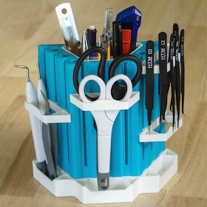 May include: A blue and white plastic tool organizer with a variety of tools, including tweezers, scissors, and pens. The organizer has a hexagonal base and a cylindrical body with slots for holding tools. The text "MO Maker 10 PRECISION TOOL ORGANIZER" is printed on the base.
