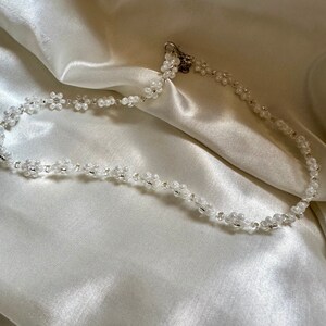 May include: A white beaded necklace with a silver clasp. The necklace is made of small, round beads that are strung together in a delicate pattern.