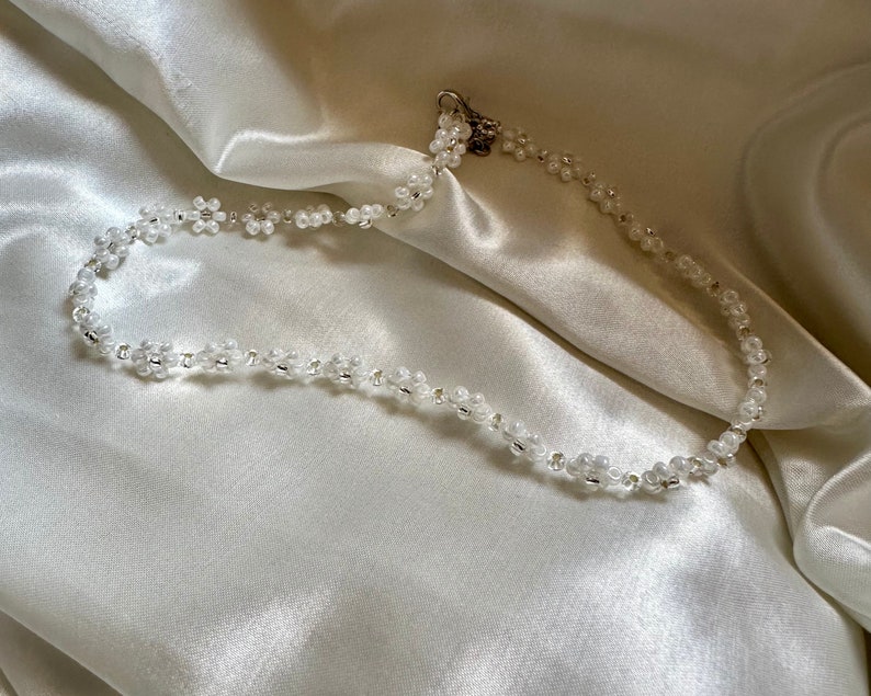 May include: A white beaded necklace with a silver clasp. The necklace is made of small, round beads that are strung together in a delicate pattern.