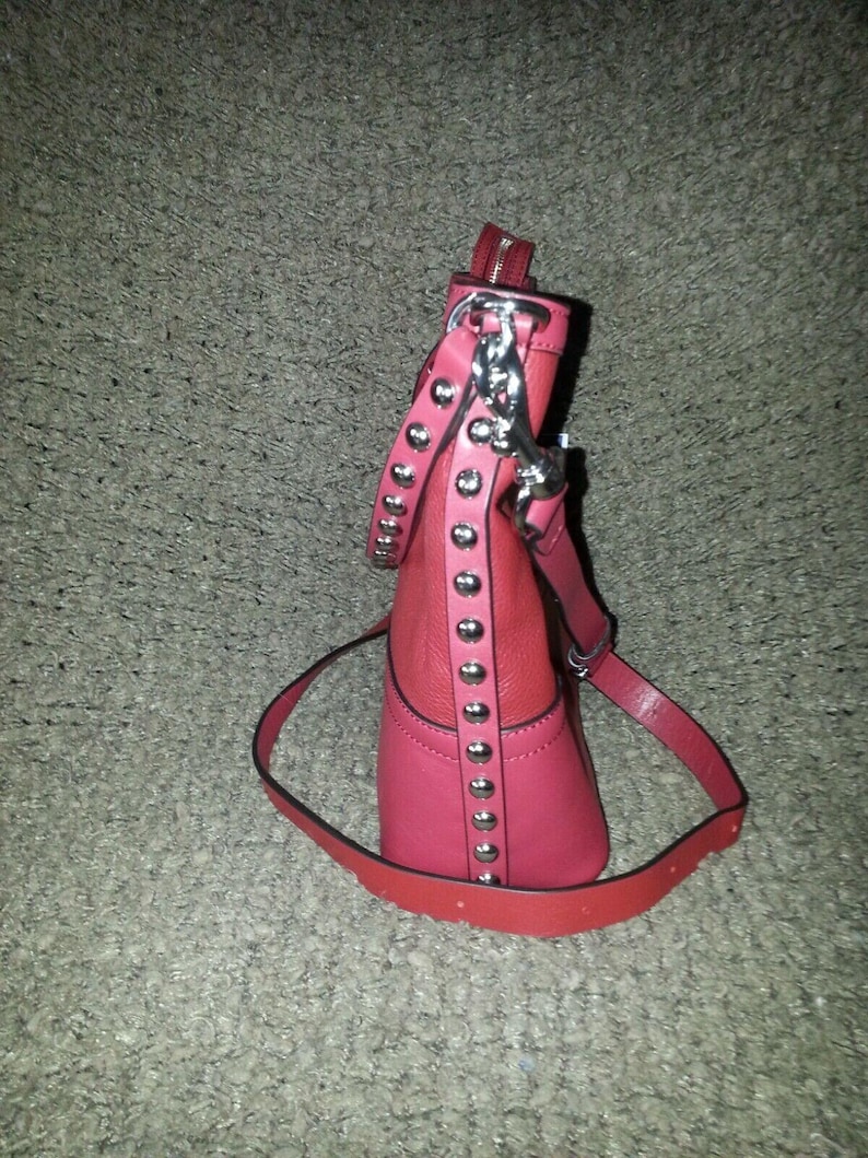 Op de afbeelding: Een tweekleurige rode en roze handtas met een verticale strook zilverkleurige metalen studs aan de zijkant. De tas is voorzien van een bijpassende rode schouderriem bevestigd met zilverkleurige hardware en een ritssluiting aan de bovenzijde.