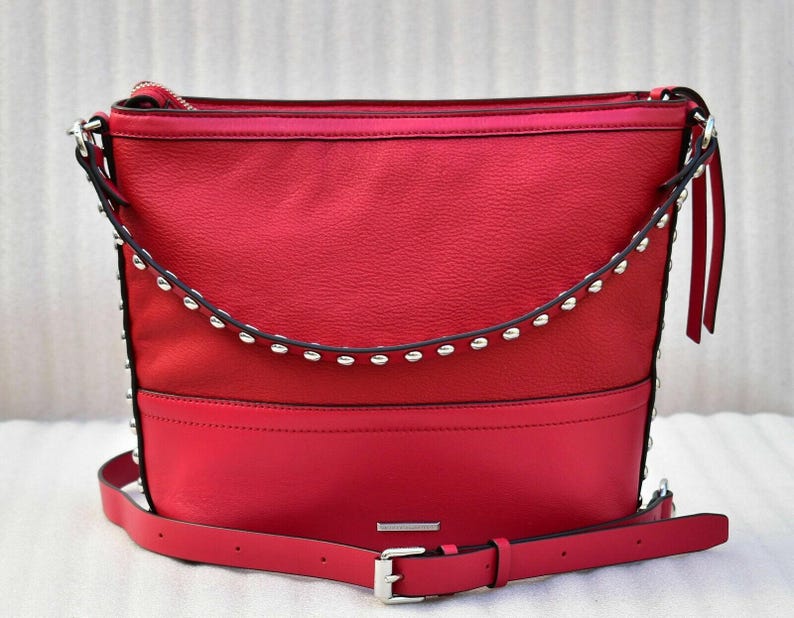 Op de afbeelding: Een felrode hobo-schoudertas met een gestructureerd bovenpaneel en een glad onderpaneel. De tas is voorzien van een gebogen band met zilverkleurige metalen studs aan de voorzijde en heeft een verstelbare schouderriem.