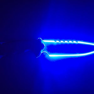 May include: A close-up of a knife with a blue glow. The blade is sharp and the handle is black.