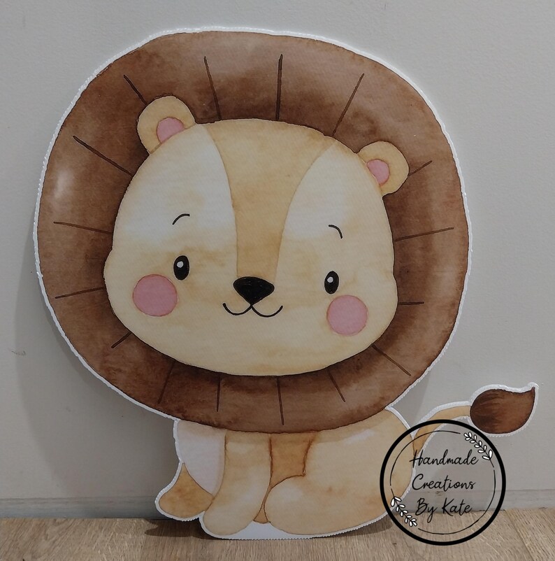 May include: A brown and tan cartoon lion with a pink nose and cheeks. The lion is sitting with its legs crossed and has a brown mane. The lion is a cutout and has a white background.
