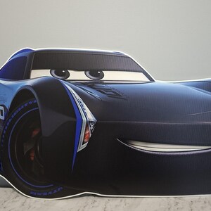 May include: A large, black and blue cartoon car cutout with the number 20 on the side. The car has large eyes and a smiling mouth. The car is a character from the movie Cars.