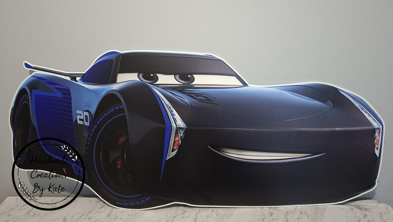 May include: A large, black and blue cartoon car cutout with the number 20 on the side. The car has large eyes and a smiling mouth. The car is a character from the movie Cars.