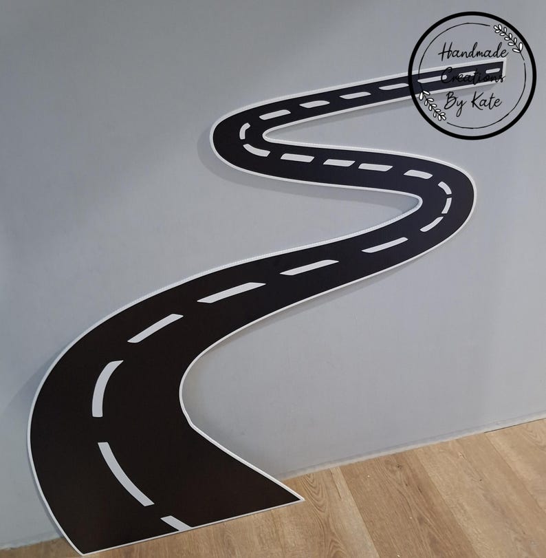 May include: A black and white road-shaped wall decal with a winding design. The road has white dashed lines and a white border. The decal is placed on a gray wall and the text "Handmade Creations By Kate" is in a circle.