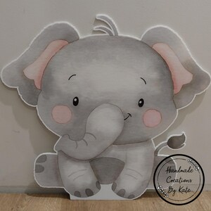 May include: A grey and pink elephant cutout with a watercolour design. The elephant is sitting with its trunk in its mouth. The cutout has a white background and a small white circle with the text "Handmade Creations By Kate".
