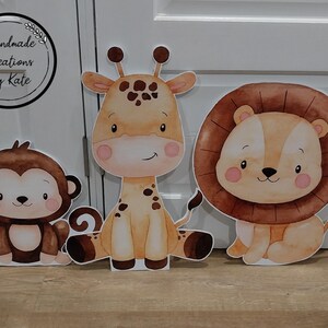 May include: Three adorable animal cutouts: a brown monkey, a brown and orange giraffe, and a brown lion with a mane. The cutouts are perfect for a jungle-themed party or nursery.