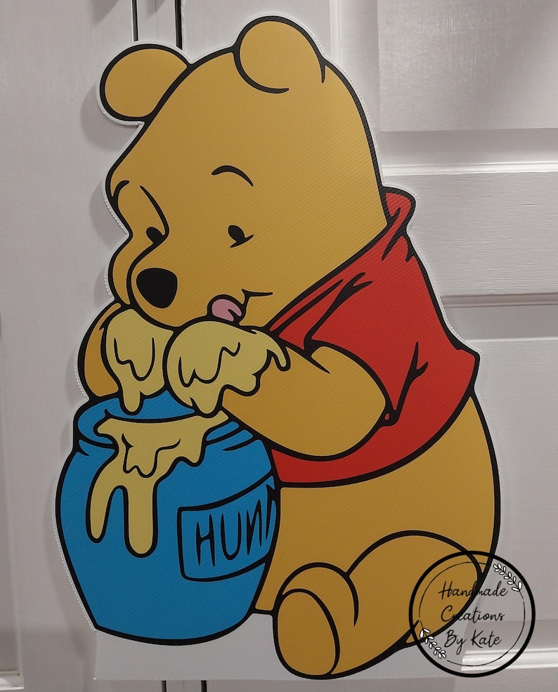 Puede incluir: Un oso de dibujos animados amarillo que lleva una camisa roja est&aacute; sosteniendo un tarro de miel azul con la palabra "HONEY" escrita en &eacute;l. El oso est&aacute; lamiendo la miel que gotea del tarro.