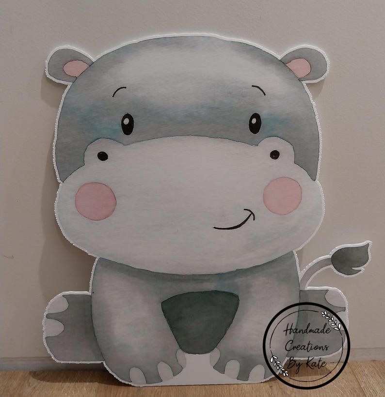 May include: A grey and white watercolour illustration of a hippopotamus with pink cheeks. The hippo is sitting with its legs crossed and has a small tail. The illustration is on a white background and includes the text "Handmade Creations by Kate".