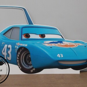 May include: A light blue cartoon car cutout with the number 43 on the side and front. The car has large eyes and a smiling mouth. The word "DINCO" is visible on the hood. The cutout has a handle on top.