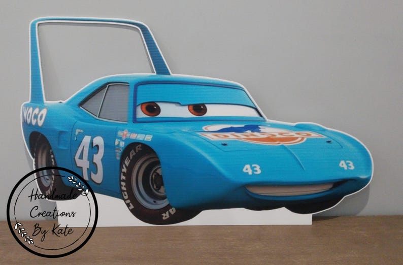 May include: A light blue cartoon car cutout with the number 43 on the side and front. The car has large eyes and a smiling mouth. The word "DINCO" is visible on the hood. The cutout has a handle on top.