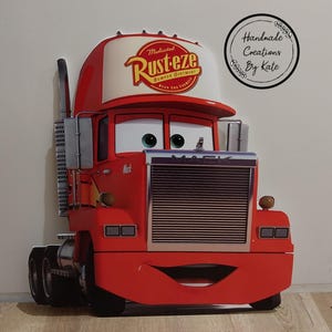 May include: A red Mack truck cutout from the movie Cars, featuring the Rust-eze logo on the cap. The truck has a smiling face, large eyes, and a chrome grill. The cutout is a handmade creation.