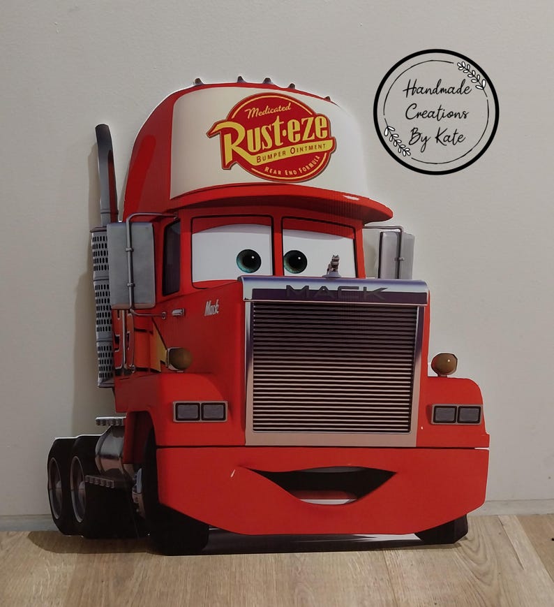 May include: A red Mack truck cutout from the movie Cars, featuring the Rust-eze logo on the cap. The truck has a smiling face, large eyes, and a chrome grill. The cutout is a handmade creation.