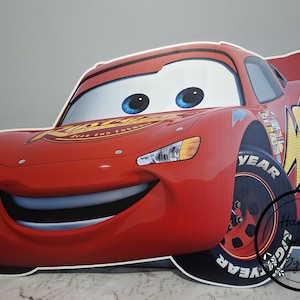 May include: A large, red Lightning McQueen cutout with a smiling face and the number 95 on the side. The car has large blue eyes and black tires with the word "YEAR" on them. The text "STAR END FORWARD" is visible on the hood.