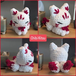 May include: A white crocheted plush toy shaped like a fox with red embroidered markings on its ears, forehead, and cheeks. The plush features closed eyes, a red bow around its neck, and a fluffy tail. The text Chibi Kitsu is visible in the center.