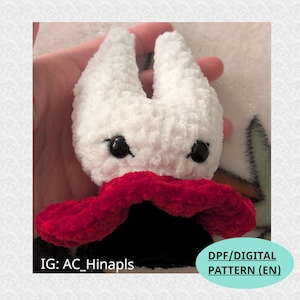 Puede incluir: Un peluche blanco hecho a mano con ojos negros y una bufanda roja. El juguete tiene un diseño único y probablemente sea un personaje de un juego o caricatura. La imagen también incluye el texto "DPF/DIGITAL PATTERN (EN)" y "IG: AC_Hinapls".