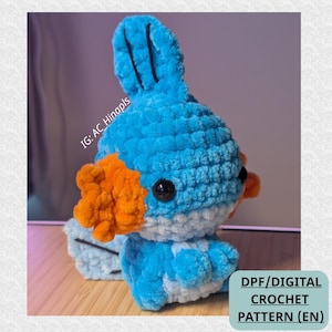 May include: A plush crochet creature featuring a bright blue head and body with a light blue underbelly, orange side gills, and a tall blue fin on top. The figure has black plastic eyes and the text IG: AC_Hinapls and DPF/DIGITAL CROCHET PATTERN (EN).